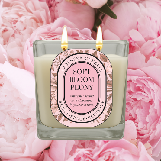 Lit Soft Bloom Peony candle by ApoThera surrounded by delicate pink peony flowers, symbolizing gentle growth, self-worth, and emotional healing.